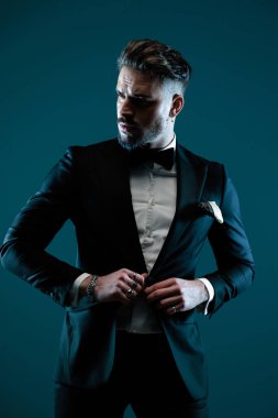 Şık sakallı bir adam smokini ayarlıyor ve kapatıyor. Bir yandan da ışıklarla poz veriyor.