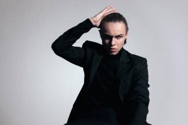 Seksi iş adamının moda resmi. Sırt kıllarını sert bir titreşimle düzeltiyor ve gri stüdyo geçmişine karşı güzel bir kıyafet giyiyor.