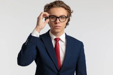 Çekici iş adamının portresi gözlüklerini takıyor ve gri stüdyo arka planına karşı resmi bir kıyafet giyiyor.