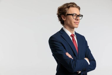 Seksi iş adamının portresi kollarını kavuşturup yan yana bakıp gülümsüyor ve gri stüdyo arka planına karşı resmi bir kıyafet giyiyor.