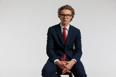 Ahşap sandalyede oturan zarif iş adamının portresi parmakları çapraz ve gri stüdyo arka planına karşı resmi bir kıyafet giyiyor.