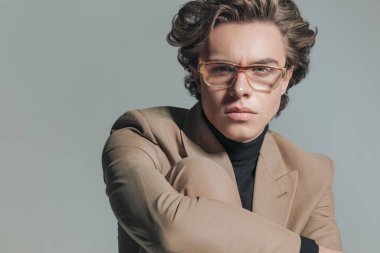 Boğazlı kazaklı yakışıklı bir gencin portresi. Stüdyoda gri arka planda koluyla dizinin etrafında poz veriyor.