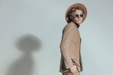 Şapkalı ve güneş gözlüklü yakışıklı genç adamın yan görünüşü. Gri arka planda el ele tutuşurken havalı bir şekilde poz veriyor.