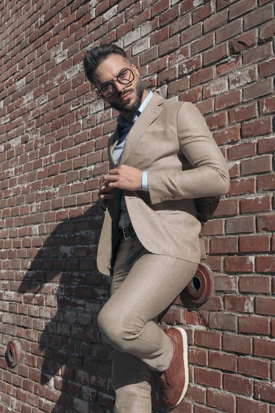 Portrait of sexy businessman leaning on wall while opening his jacket and wearing eyeglasses outdoor, in an old medieval town