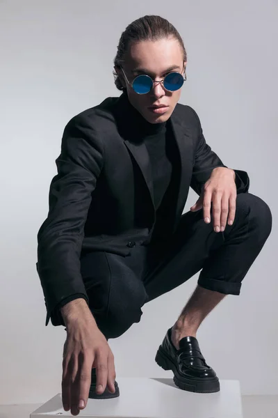 Fashion picture of sexy businessman squatting with tough vibe and wearing a nice outfit against gray studio background