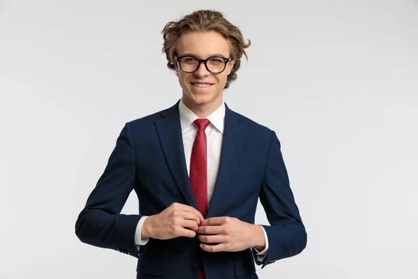 若い実業家の肖像は彼のスーツのジャケットを閉じて笑顔を与え 灰色のスタジオの背景に対して正式な衣装を着て — ストック写真