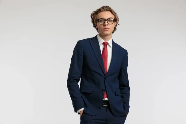 若いビジネスマンの肖像画は ポケットに彼の手でポーズとグレーのスタジオの背景に対して正式な衣装を着て — ストック写真