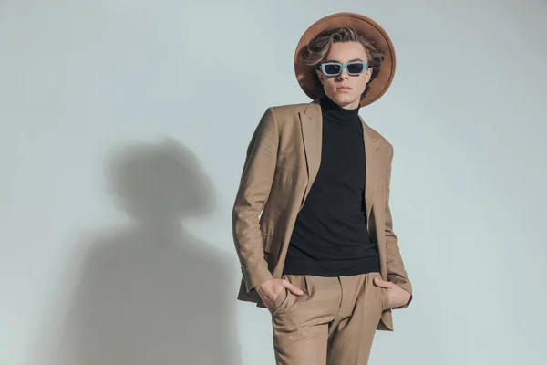セクシーなファッション男とともに帽子とサングラスを手でポケットに入れる前にグレーの背景でスタジオ — ストック写真