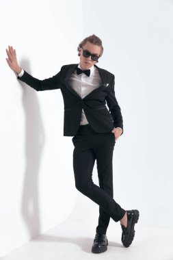 Uzun saçlı, zarif bir sağdıç. Bir eli duvarda, diğeri cebinde ve kendine güvenen bir şekilde poz veriyor.