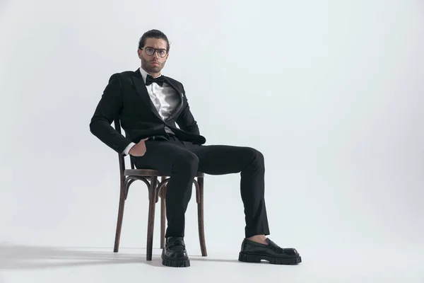 Elegancki Atrakcyjny Mężczyzna Okularach Siedzący Rękami Kieszeniach Przed Szarym Tłem — Zdjęcie stockowe
