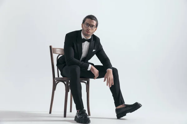 时尚男人 戴着眼镜 双膝肘部坐着 在灰色背景前摆姿势 — 图库照片