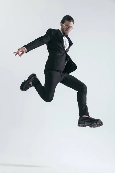穿着黑色燕尾服的活泼优雅的男人跳到空中 在灰色的背景中以冷静的方式摆姿势 — 图库照片