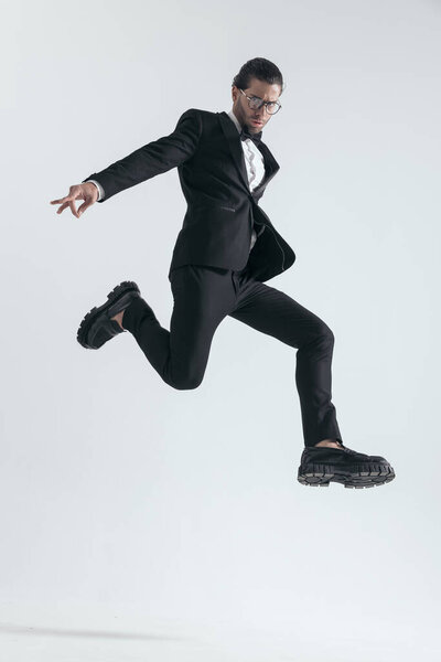 dynamic elegant man in black tuxedo jumping in the air and posing in a cool way on grey background
