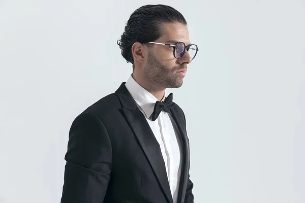 性感优雅的男人 戴着黑色燕尾服的眼镜 面朝一边 在灰色背景前摆姿势 — 图库照片
