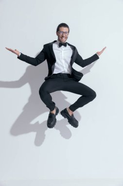 Havaya çömelmiş, gülen, beyaz stüdyo arka planına karşı gözlük takan zarif bir iş adamı.