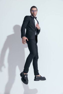 Smokinini tamir ederken atlayan çekici bir iş adamı, beyaz stüdyo geçmişine karşı gözlük takıyor.