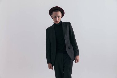 Çekici iş adamının moda fotoğrafı kameraya sert bir bakış atıyor ve gri stüdyo arka planına karşı şık bir kıyafet giyiyor.