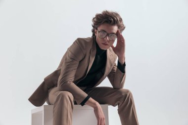 Genç işadamının portresi öne eğiliyor ve alnına dokunuyor ve gri stüdyo arka planına karşı resmi bir kıyafet giyiyor.