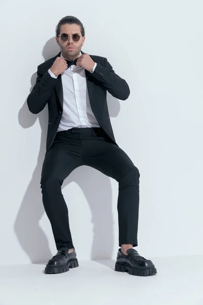 stock image elegant businessman with tough attitude arranging his bowtie, wearing glasses against white studio background