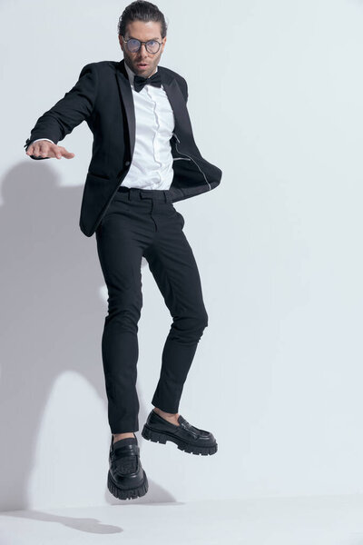 elegant businessman jumping and dominating the frame, wearing glasses against white studio background