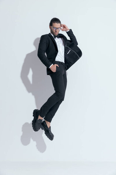 sexy businessman jumping with hands in pockets and fixing glasses, wearing glasses against white studio background