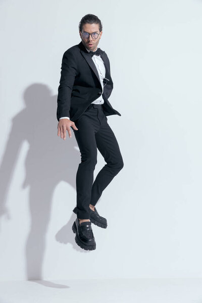 young businessman jumping and posing in the air, wearing glasses against white studio background