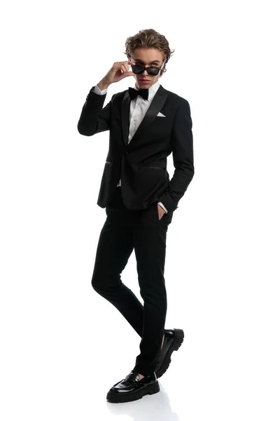 セクシーなビジネスマンがリラックスした姿勢でサングラスをかけて白いスタジオの背景に正式な衣装を着て — ストック写真