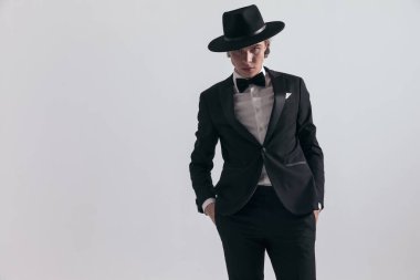 Siyah smokinli şık bir moda adamı. Stüdyonun gri arka planının önünde el ele tutuşup el ele tutuşuyor.