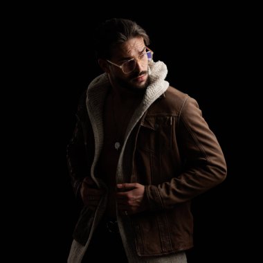 Yün hırka ve ceketi ayarlayan kendine güvenen ve siyah arka planda havalı bir poz veren bir adam.