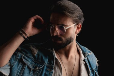 Moda portresi kot ceketli genç adam yan bakmak ve siyah arka plan önünde gözlük ayarlama