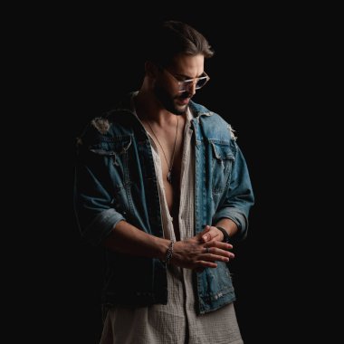 Avuç içleri gözlüklü, siyah arka planda gizemli bir şekilde poz veren baştan çıkarıcı bir gencin portresi.