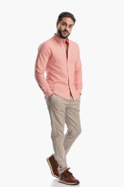 Stüdyoda, beyaz arka planda elleri ceplerinde, şık ve rahat giyinen seksi genç adam.