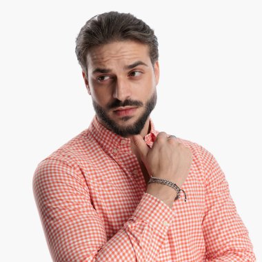 Ekose gömlekli çekici bir adam. El ele tutuşup stüdyoda beyaz bir arkaplanın önüne bakıyor.