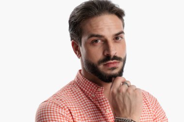 Sakallı, ekose gömlekli, el ele tutuşan ve beyaz arka planda poz verirken düşünen düşünceli bir gencin portresi.