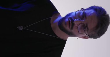 Gözlüklü seksi adam sakala dokunuyor ve polis ışıkları açık gri arka plandayken etrafta dolanıyor.