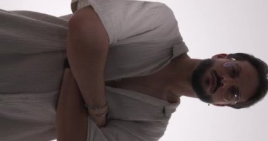 Tişörtlü, gözlüklü, kollarını kıvıran, dudaklarına dokunan, tişörtünü ayarlayan, açık gri arka planda spot ışığı altında duran seksi moda adamı.