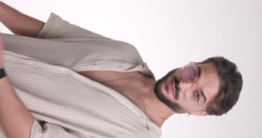 Gözlüklü seksi genç adam gömleğini düzeltirken gülümsüyor, beyaz arka planda flört ederken kendine güveniyor ve karşı konulmaz oluyor.