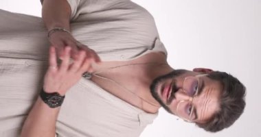 Sıradan sakallı bir adamın el ele tutuşup stüdyoda beyaz arkaplan önünde poz verirken onları öne doğru gösterdiği dikey bir video.
