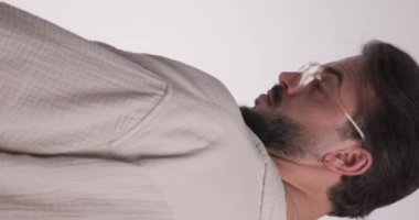 Gözlüklü ve ileriye bakan çekici genç adamın videosunu kapat. Sakalı düzeltip açık gri arkaplan önünde düşünürken.
