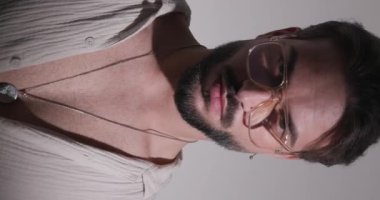 Gözlüklü seksi sakallı adam, kamera stüdyoda siyah arka planda göğsünü gösterirken aşağı bakıyor.