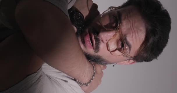 一个没有刮胡子的男人 戴着眼镜 手挽手 在灰色背景前拥抱自己的垂直视频 — 图库视频影像