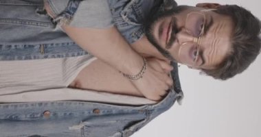 Gözlüklü seksi genç adam omuzlarını ve göğsünü gösteriyor. Gri arka planda esniyor ve poz veriyor.
