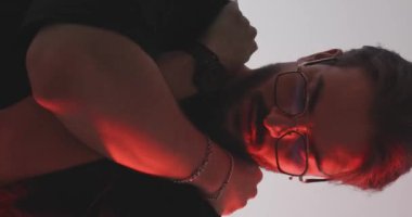 Gri arka planda polis ışıkları açıkken, kollarını kaldırıp sarılan, ileriye ve yana bakan tehlikeli sıradan bir adam.