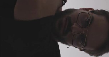 Gri arka planda bir aşağı bir yukarı bakarken gözlüklü genç bir adamın kollarını tutarak sarılışının polis ışıkları açık olduğu dikey bir video.
