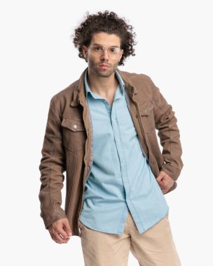 Gözlüklü, bej ceketli ve beyaz arka planda poz veren seksi bir adam. 