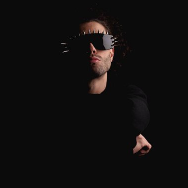 Havalı güneş gözlüklü kibirli bir gencin portresi. Stüdyoda siyahların önünde kendinden emin duruyor.