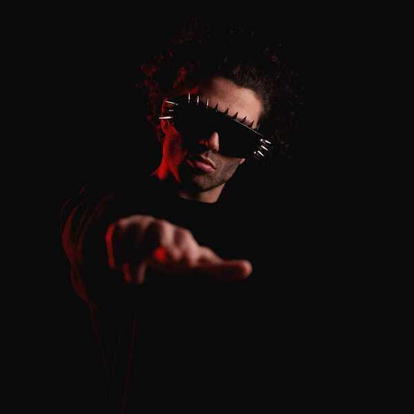 portrait of curly hair man with cool sunglasses making hand gesture and pointing finger forward in front of black background with red lights on