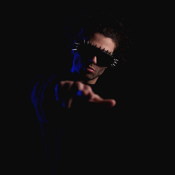 portrait of fashion cool man with cool glasses pointing fingers to camera and being confident while police lights are on in front of black background
