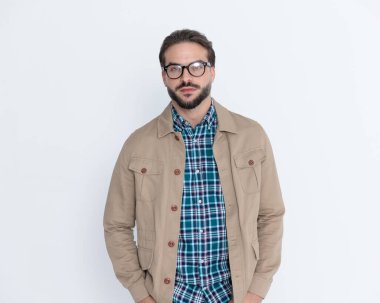 Ekose gömlekli, ceketli, cebinde el ele tutuşan ve gri arka planda poz veren seksi, sıradan bir adam.