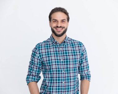 Casul ekose gömlekli mutlu genç adam ileriye bakıyor ve gri arka planda gülümsüyor.